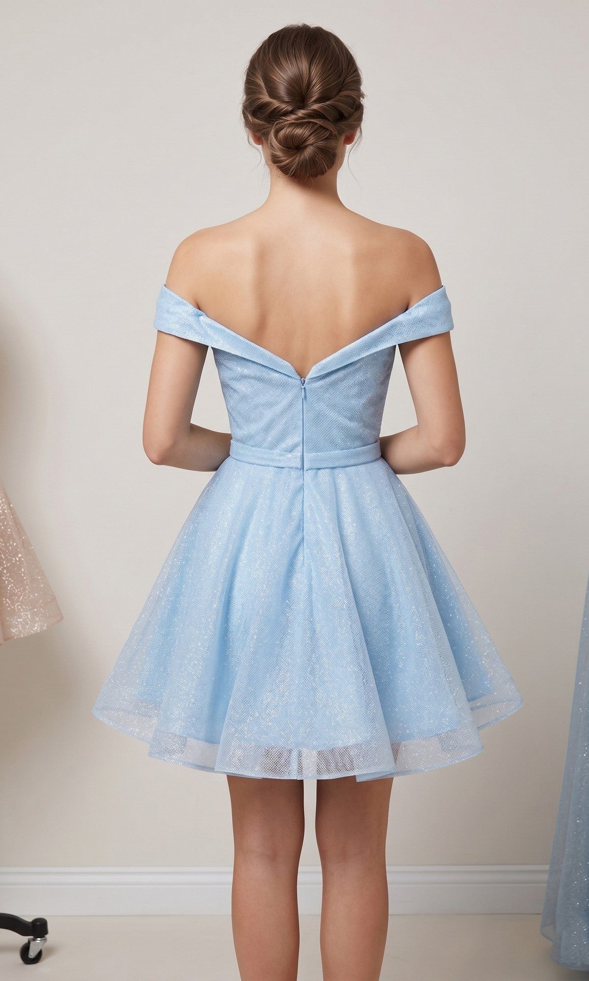 A woman stands facing away, her hair styled in a neat low bun, wearing the Chicas C323 Short Homecoming Dress—an off-the-shoulder, light blue fit-and-flare dress with a flared skirt.
